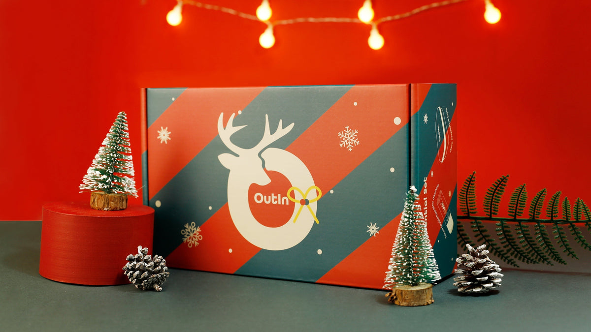 OutIn Nano schwarze tragbare Espressomaschine mit Weihnachtsgeschenkbox, Kaffeekapseln, Mini-Weihnachtsbaum und Lichterkette auf rotem Hintergrund