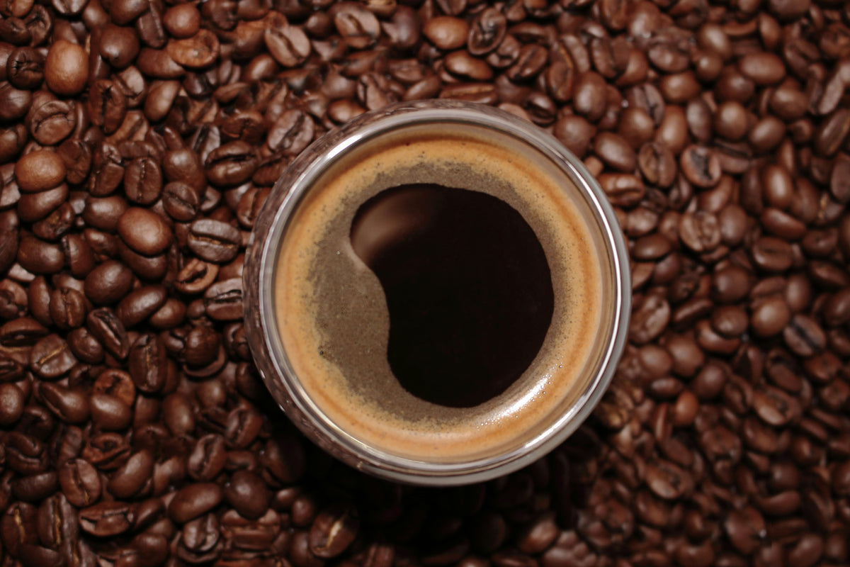 Obenansicht einer Espressotasse mit goldener Crema, umgeben von ganzen Kaffeebohnen – Fokus auf Aroma, Röstung und Frische.