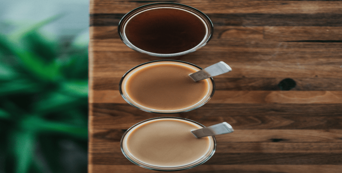 Drei Tassen Kaffee in unterschiedlichen Farbtönen – von dunkel bis hell – als Vergleich von Röstgrad, Milchanteil und Stärke auf Holztisch.
