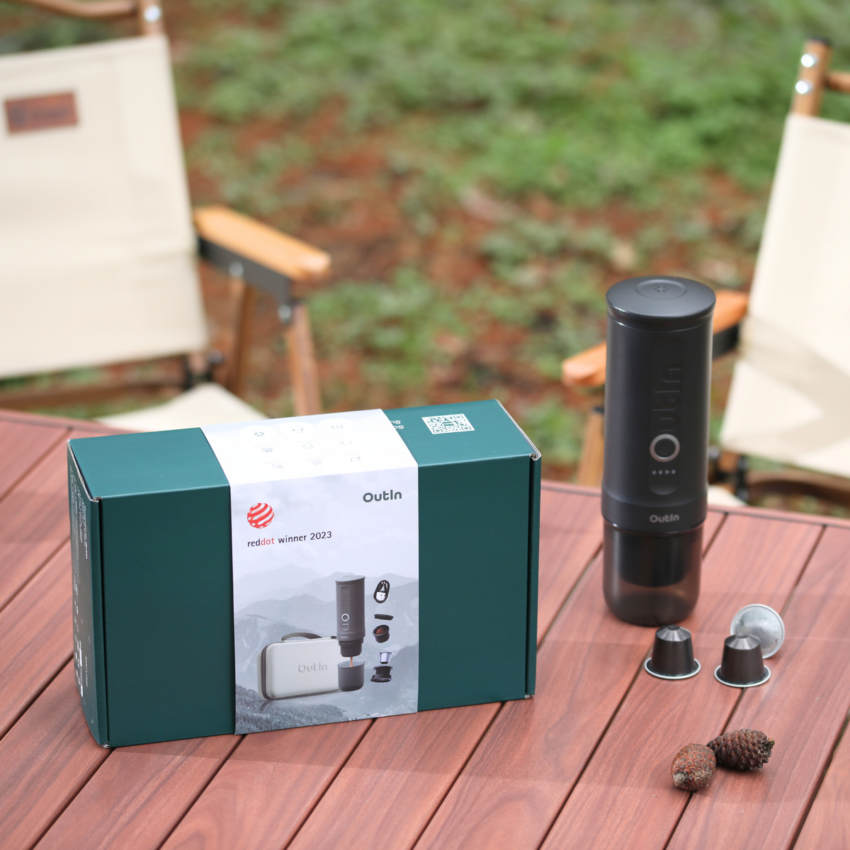 OutIn Espresso-Geschenkset Space Grau mit Red Dot Award 2023, Zubehör und Kapseln auf Holztisch im Freien.