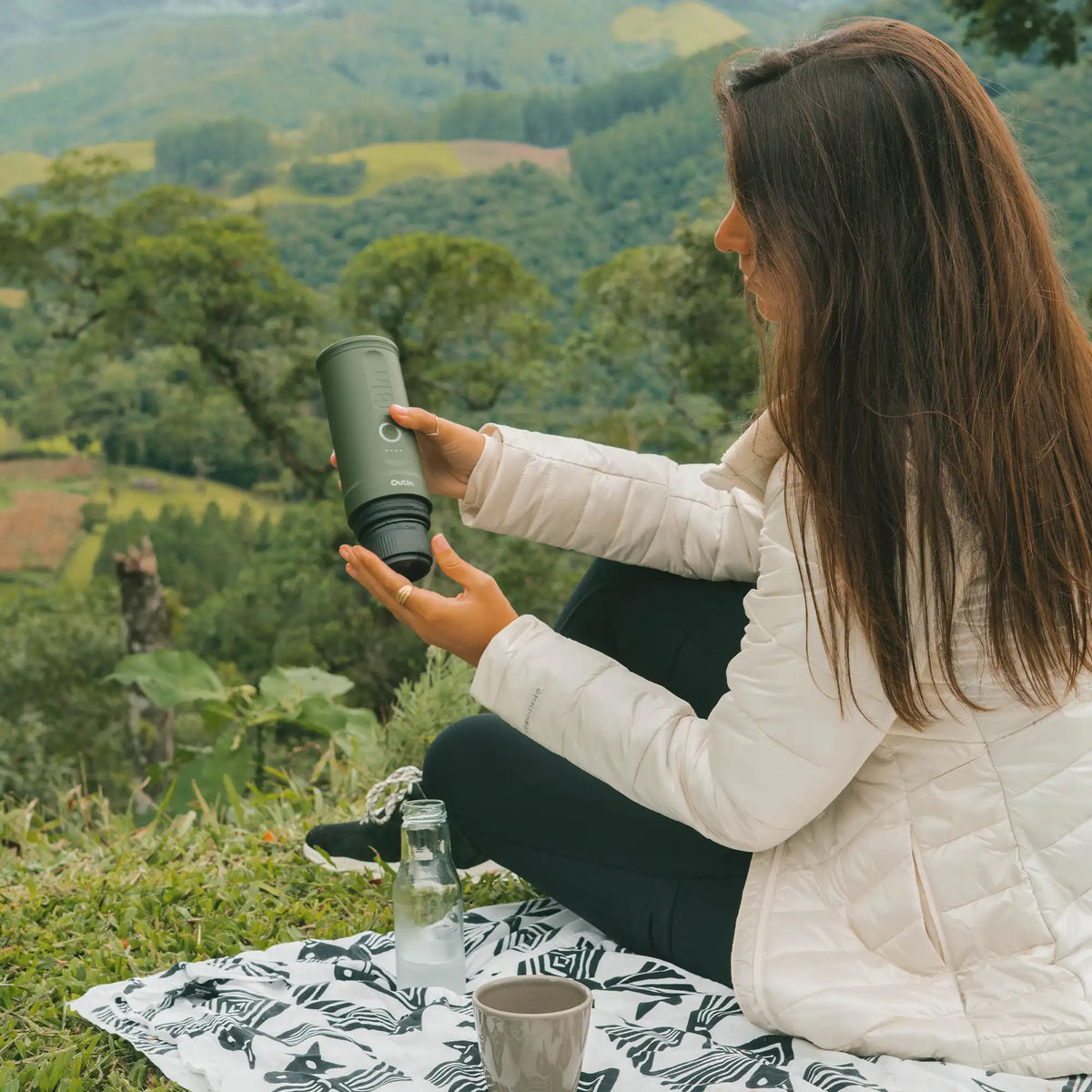Frau hält waldgrüne OutIn Nano Espressomaschine im Freien, ideal für Camping und Reisen.