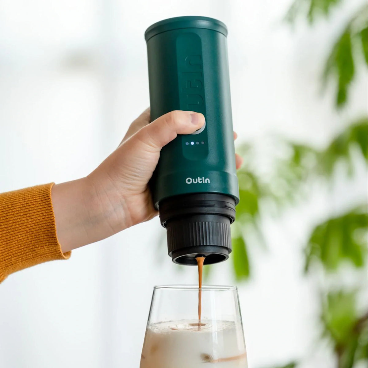 Nano tragbare Espressomaschine blaugrün mit OutIn Logo brüht Espresso in ein Glas mit Eis und Milch.