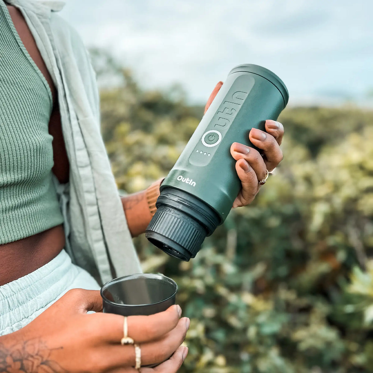 Waldgrüne OutIn Nano Espressomaschine für unterwegs in Gebrauch im Freien, mit Tasse und Logo.