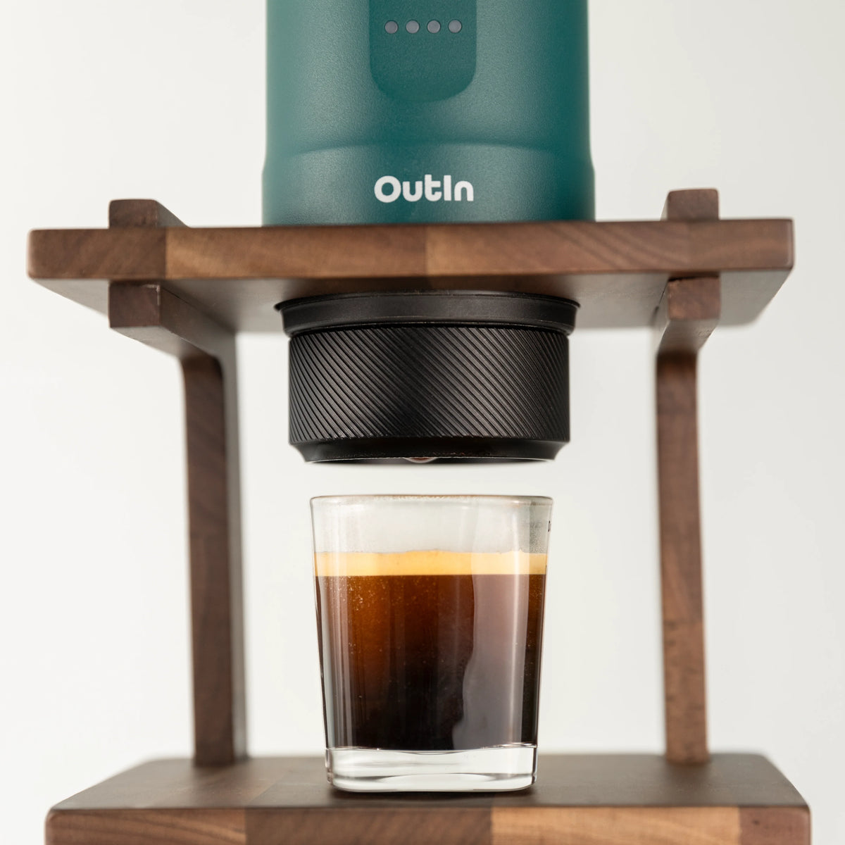 Grüne OutIn Nano Espressomaschine brüht doppelten Espresso mit Crema in Glas auf Holzständer.