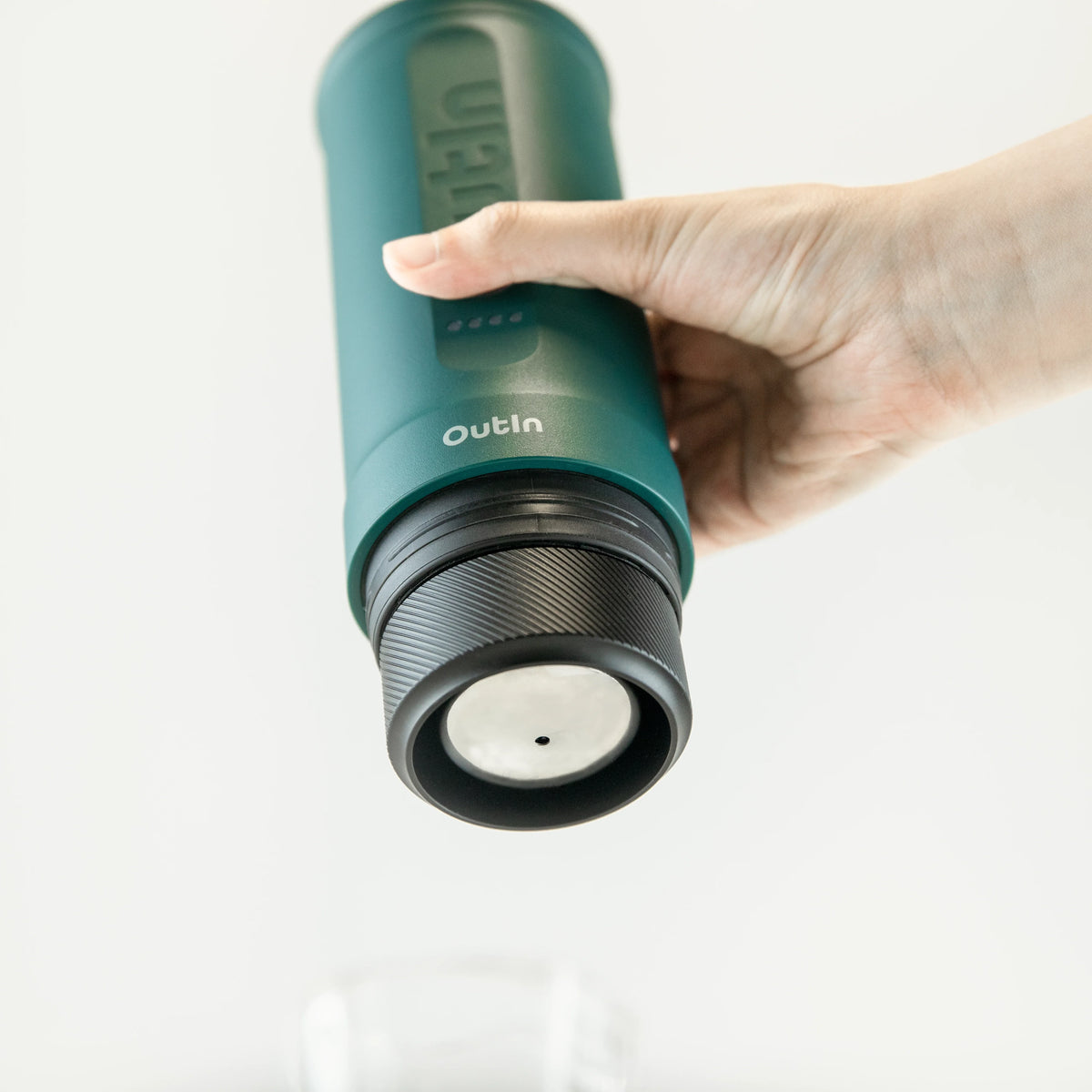 Smaragdgrüne OutIn Nano Espressomaschine von Hand gehalten über Glas für Espresso-Zubereitung.