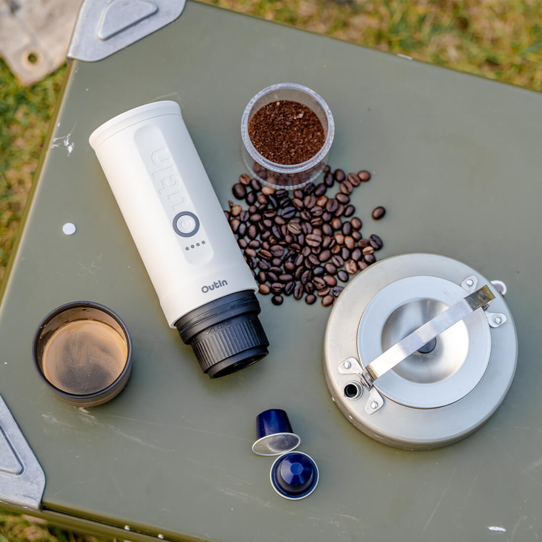 Perlweiße OutIn Nano Espressomaschine mit Kaffeebohnen, Kapseln, Espresso und Wasserkocher für Kaffee unterwegs.