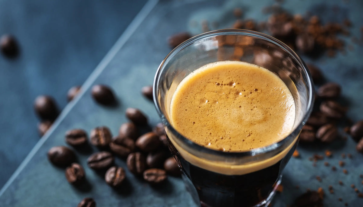 Frischer Espresso mit goldener Crema im Glas und Kaffeebohnen auf Tisch
