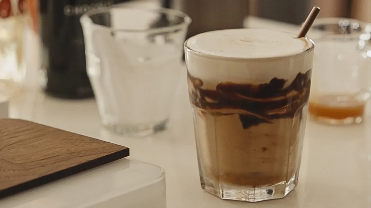 Eine Nahaufnahme eines Eiskaffees in einem facettierten Glas, gekrönt von Schaum und Schokoladensauce, mit einem Trinkhalm