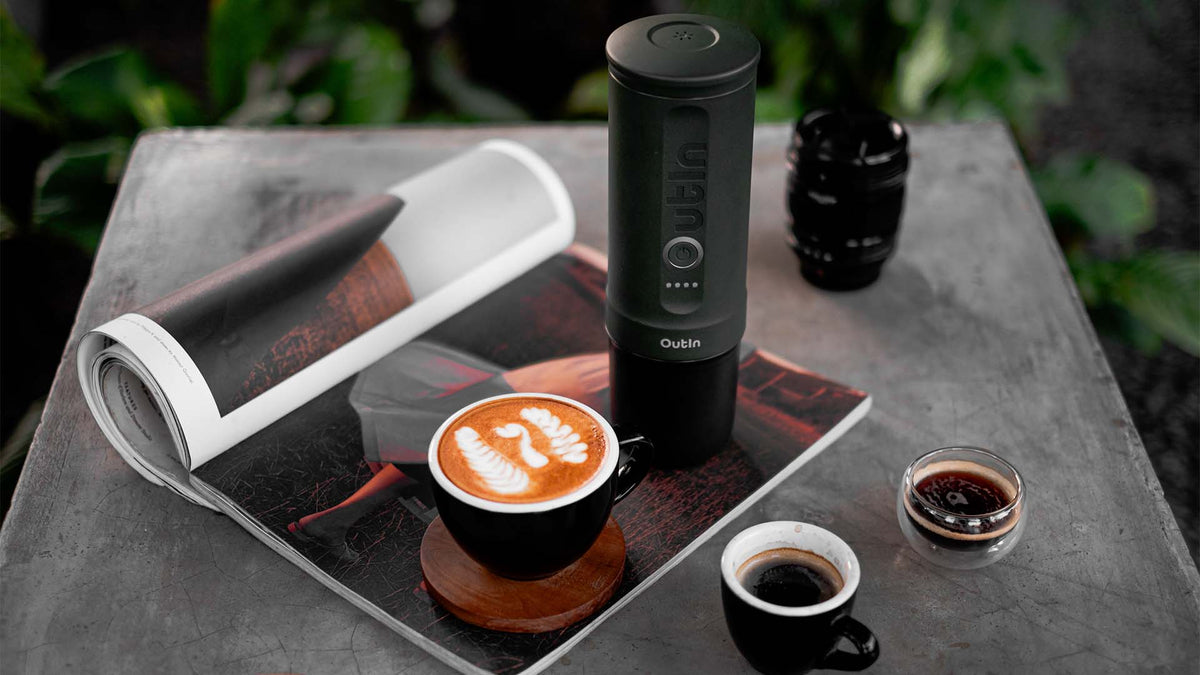 Outin Espressobereiter mit sichtbarem Logo neben einem Latte mit Latte Art auf einem Kaffeetisch