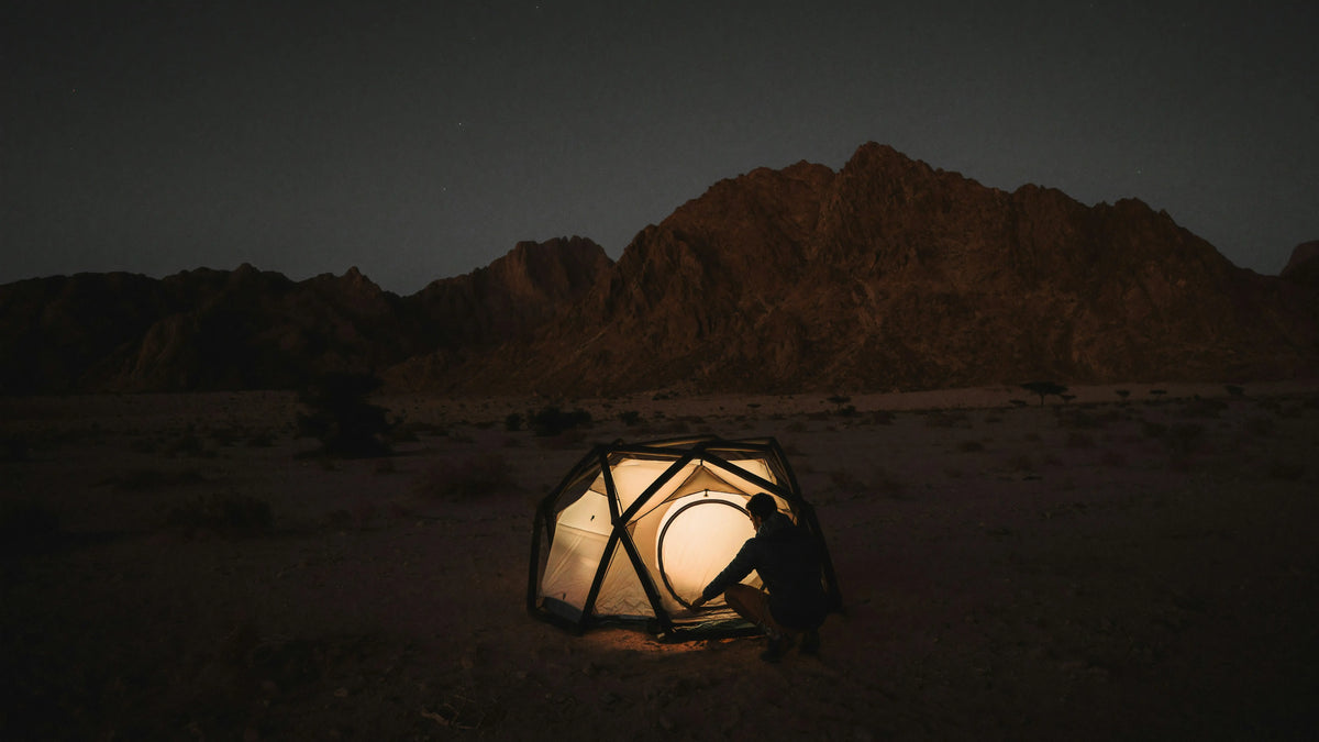 Nachtcamping in der Wüste – beleuchtetes Zelt vor felsiger Bergkulisse, ruhige Outdoor‑Atmosphäre
