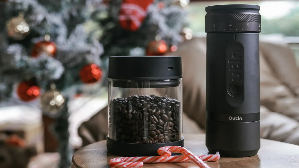 Outin elektrische Kaffeemühle und Vakuumbehälter mit frischen Kaffeebohnen, arrangiert vor festlicher Weihnachtsdekoration und Zuckerstangen﻿