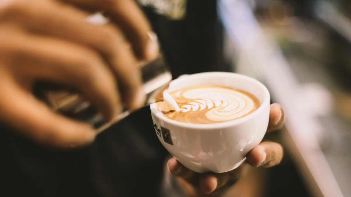 A person holding a cup of cappuccino with latte art design on the foam.