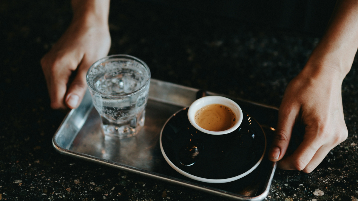 Perfekter Ristretto-Espresso in einer schwarzen Tasse mit Sprudelwasser auf einem Metalltablett, der das ideale konzentrierte Shot-Volumen von 15–20 ml zeigt