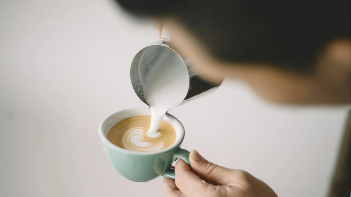 Aufgeschäumte, fettarme Milch wird in eine mintgrüne Tasse gegossen, um Latte Art zu kreieren. Dies demonstriert die richtige Technik zur Zubereitung eines Skinny Latte mit der Textur von cremigem Mikroschaum