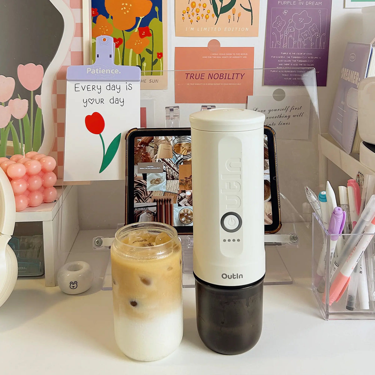 Perlweiße OutIn Nano Espressomaschine neben Eiskaffee auf einem Schreibtisch, ideal für Kaffee unterwegs.