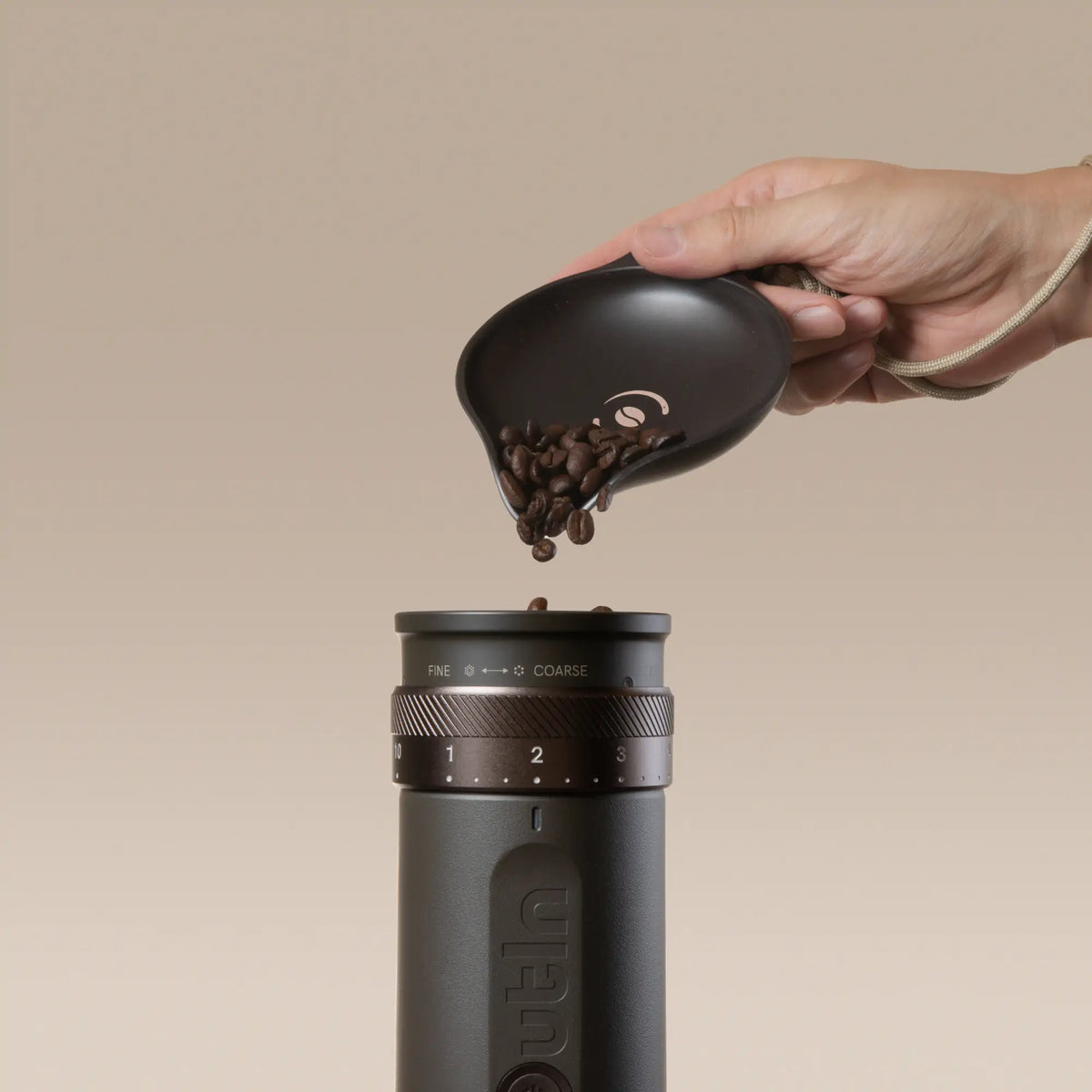OutIn Rebrew Bohnen-Tablett dunkelbraun mit Kaffee-Logo füllt Kaffeebohnen in Mühle für Mahlprozess, mit beigem Lanyard.