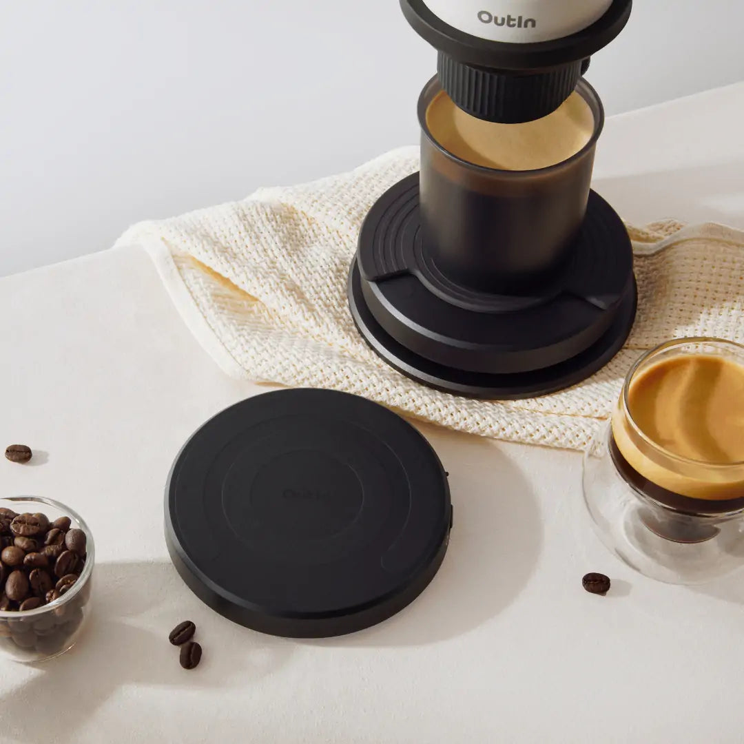 Schwarze OutIn Claro Kaffeewaage mit Espressozubereiter, Kaffeebohnen und Silikonmatte.