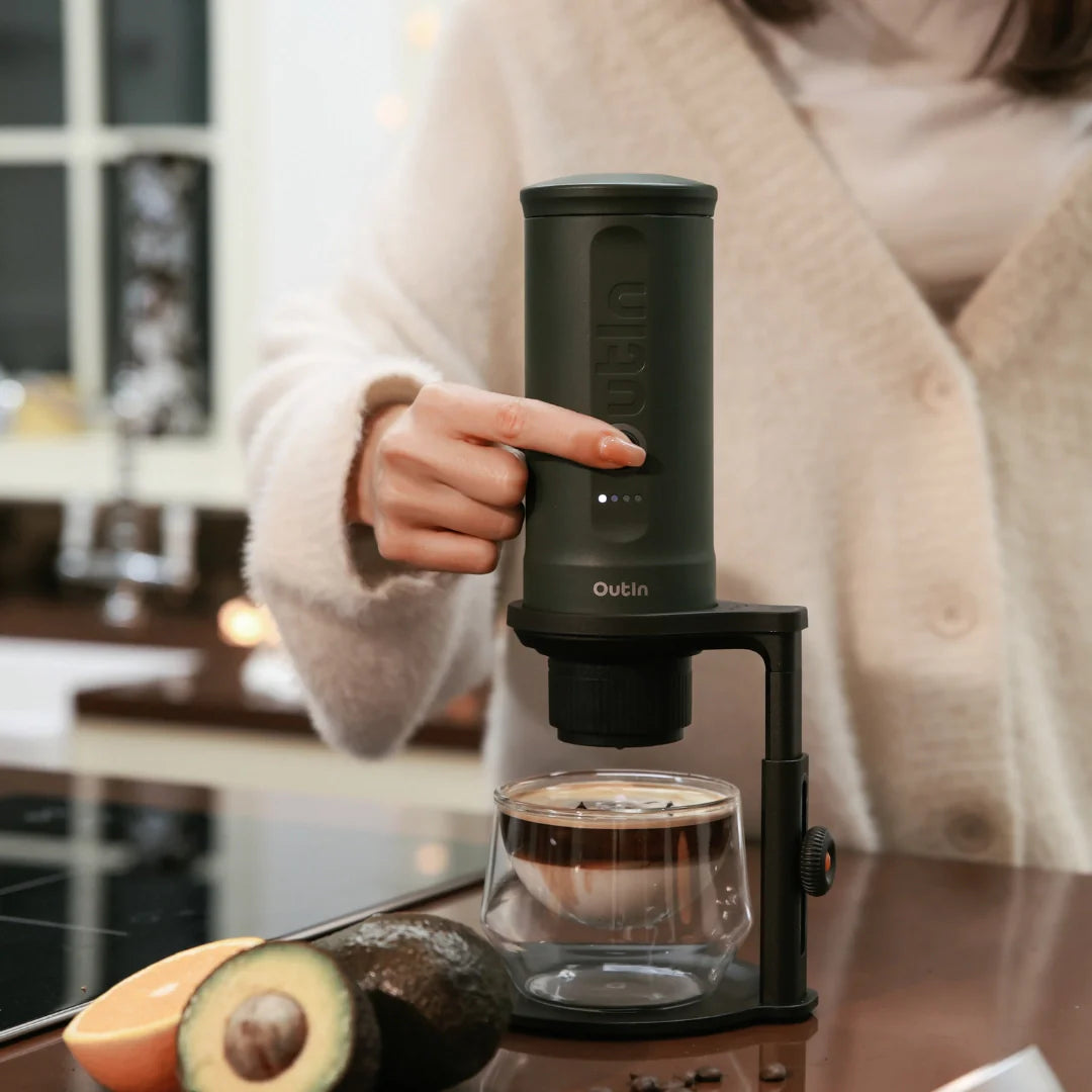 Person brüht Kaffee mit OutIn Kaffeeständer und doppelwandigem Glas, Höhe verstellbar, heimeliges Ambiente.