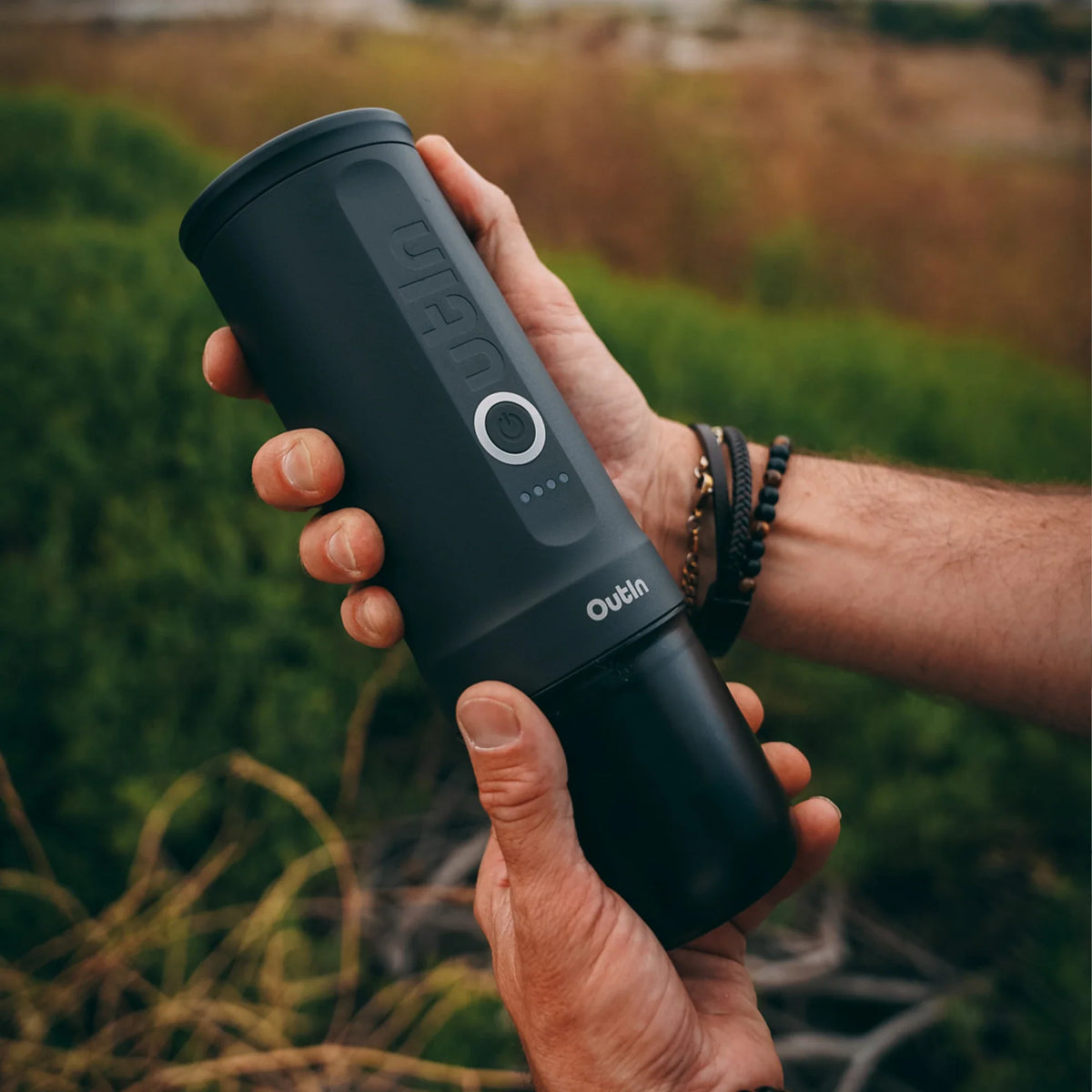 Person hält OutIn Nano Tragbare Espressomaschine in Space Grau im Freien, ideal für Camping und Reisen.