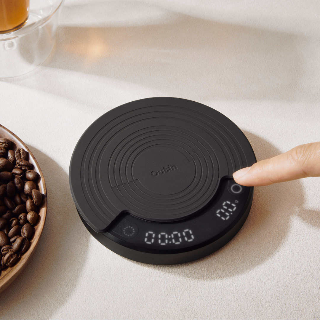 OutIn Claro Kaffeewaage, schwarzer runder Design, eine Hand bedient Knopf, Display zeigt 00:00/0.0.