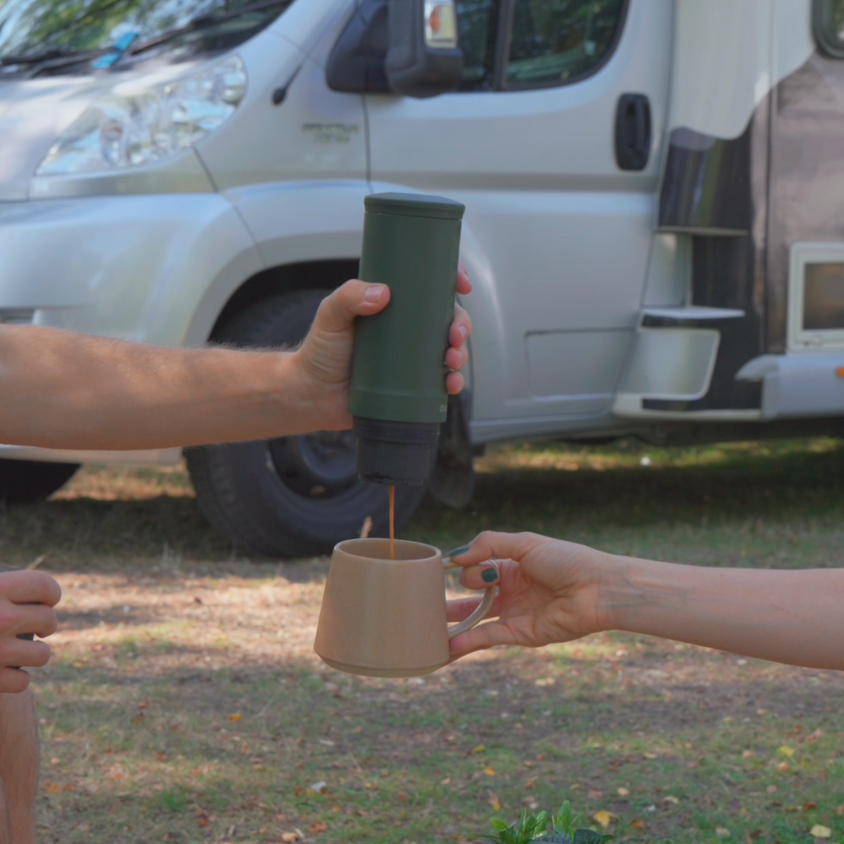 Waldgrüne OutIn Nano Espressomaschine brüht Kaffee im Freien vor Wohnmobil in Becher.