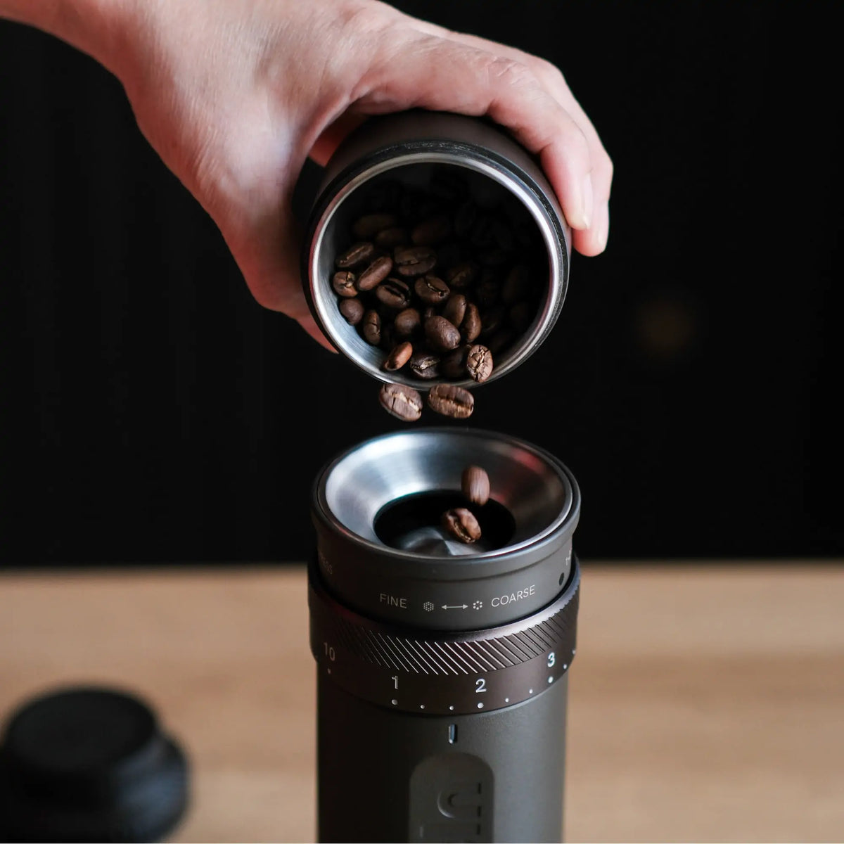 OutIn Fino Kaffeemühle: Hand füllt Kaffeebohnen in tragbare elektrische Kaffeemühle mit Mahlgradskala.