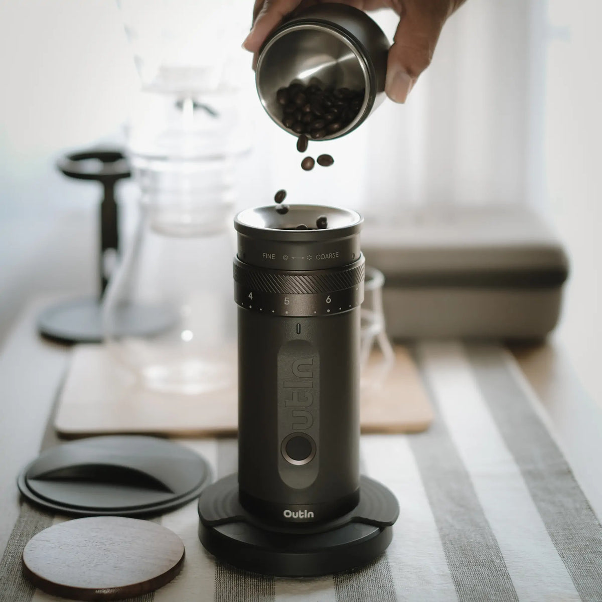 OutIn Fino Kaffeemühle: Hand füllt Kaffeebohnen in schwarze elektrische Mühle mit Mahlgradskala.
