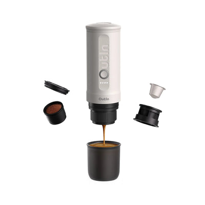 Perlweiße OutIn Nano Espressomaschine brüht Espresso in Becher; Zubehör für Kapseln und gemahlenen Kaffee schwebt daneben.