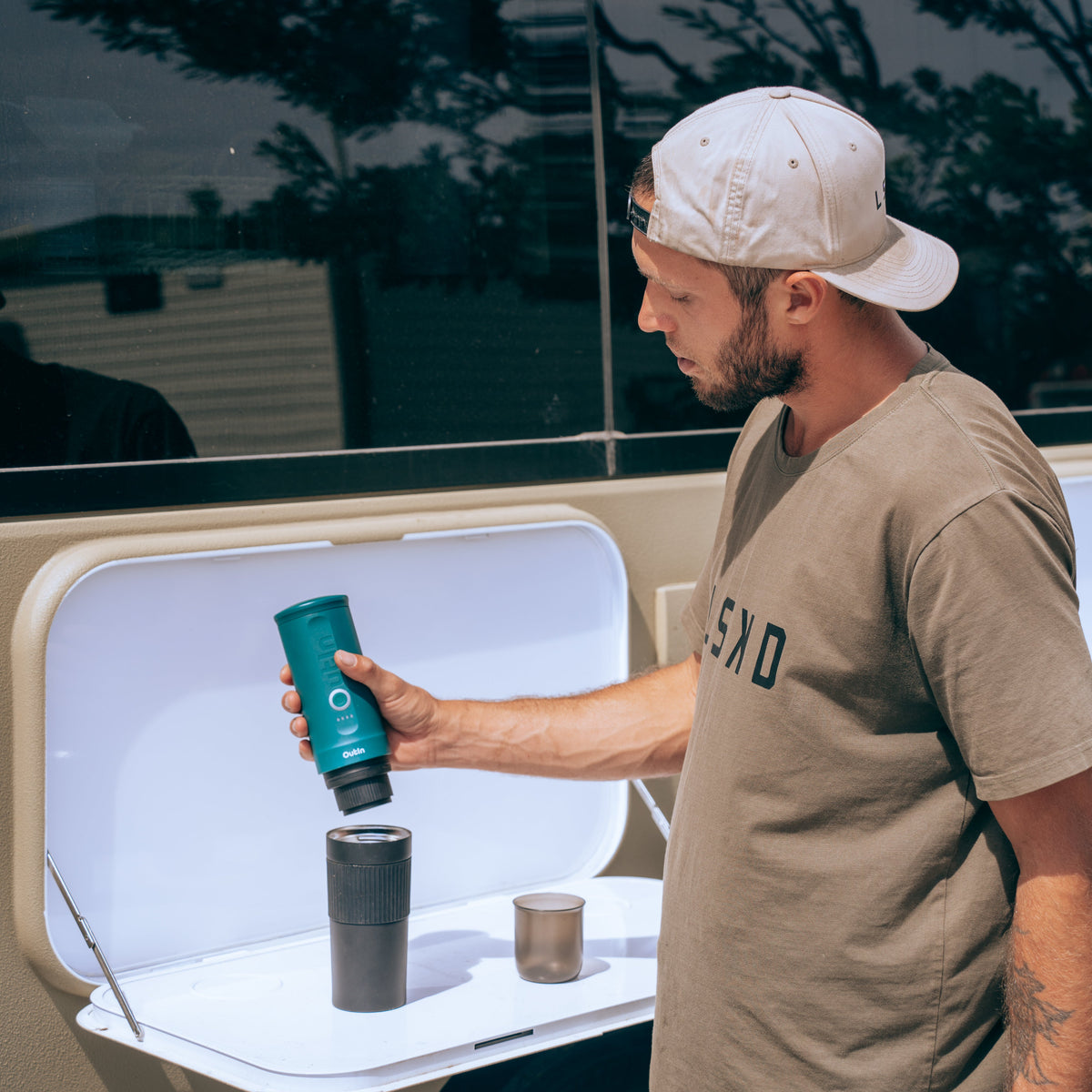 Mann benutzt blaugrüne Nano Tragbare Espressomaschine mit Kaffeemaschine auf einem Klapptisch im Freien.