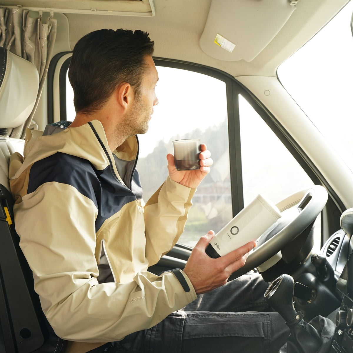 Mann genießt Kaffee im Auto mit perlweißer OutIn Nano Espressomaschine und Becher.