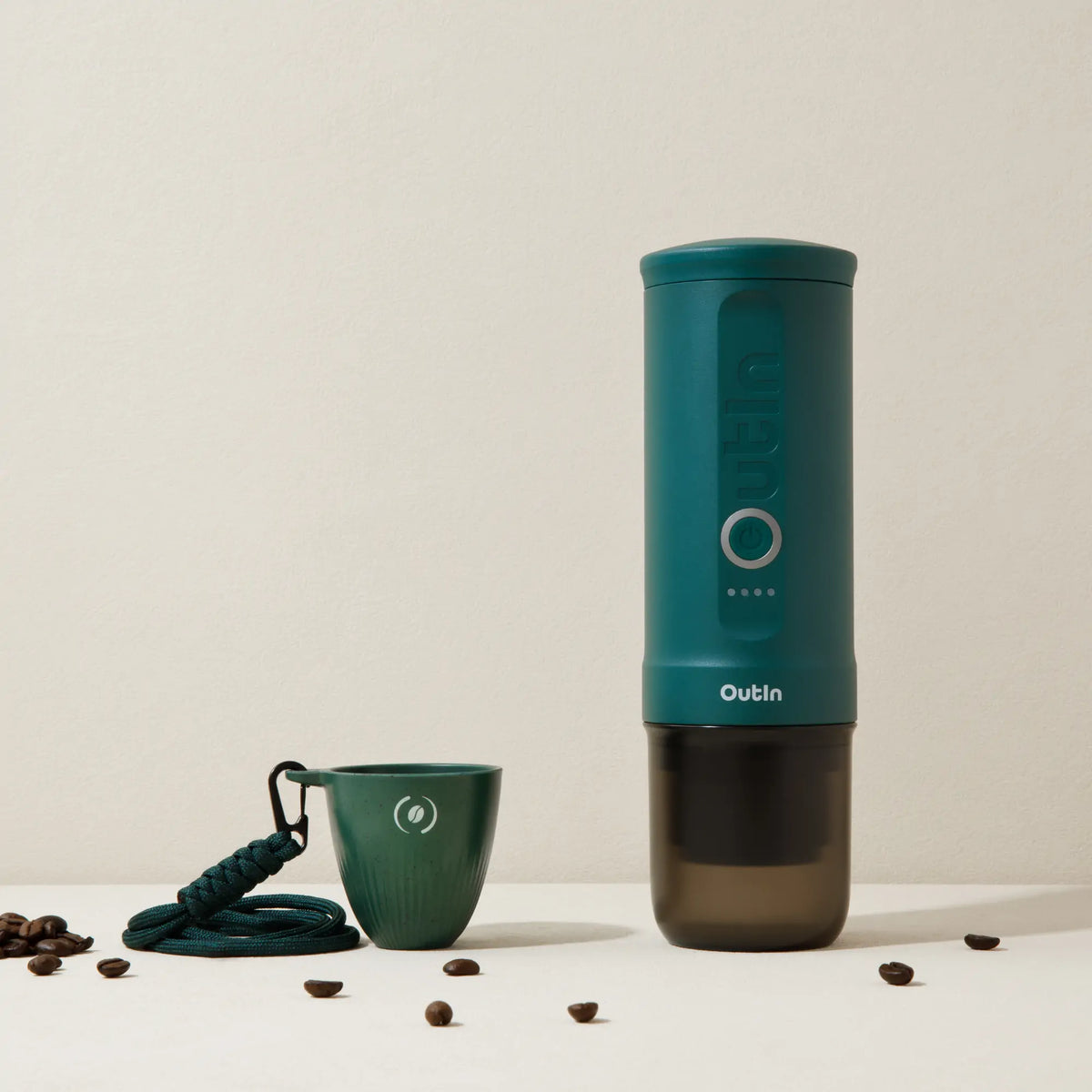 Dunkelgrüner OutIn Rebrew Espressobecher mit Lanyard und Kaffeebohnen-Logo, neben OutIn Nano Maschine und Kaffeebohnen.